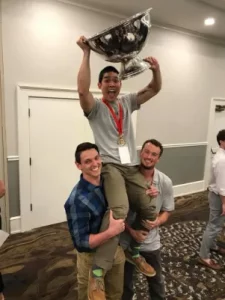 Joe being lifted on peers' shoulders with larger trophy